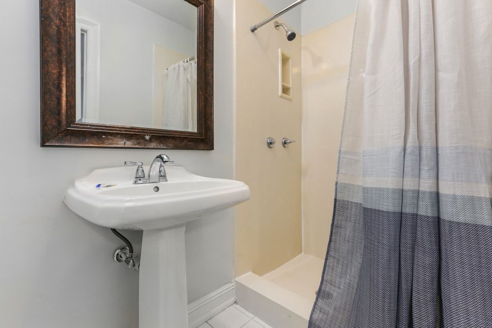A bathroom with a white sink, a mirror with a wooden frame, a shower with a beige door, and a striped shower curtain.