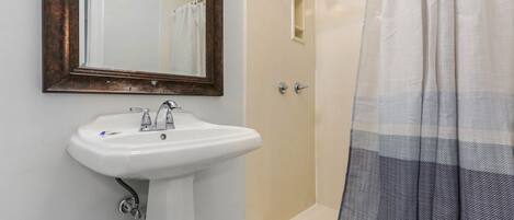 A bathroom with a white sink, a mirror with a wooden frame, a shower with a beige door, and a striped shower curtain.