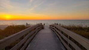A wooden boardwalk leading to a beach with a sunset in the background. - Ocean Dreaming: Waterfront Home with Heated Pool, New Dock and Amazing Sunsets! (Indian Rocks Beach)
