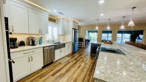 A modern kitchen with white cabinets, stainless steel appliances, and a marble countertop. - Ocean Dreaming: Waterfront Home with Heated Pool, New Dock and Amazing Sunsets! (Indian Rocks Beach)