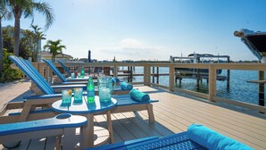 A wooden deck with lounge chairs and tables, overlooking a marina with boats. - Ocean Dreaming: Waterfront Home with Heated Pool, New Dock and Amazing Sunsets! (Indian Rocks Beach)
