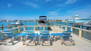 A deck with lounge chairs and tables overlooking a marina with boats. - Ocean Dreaming: Waterfront Home with Heated Pool, New Dock and Amazing Sunsets! (Indian Rocks Beach)