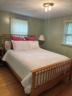 Habitación individual con una cama de madera, mesita de noche, lámpara y ventana con persianas.
