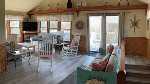 Ein gemütliches Wohnzimmer mit Kamin, Fernseher und einem großen Fenster mit Blick auf eine Terrasse.