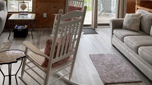Ein geräumiges Wohnzimmer mit Deckenventilator, einem Schaukelstuhl, einer Couch und Blick auf die Terrasse.