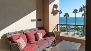 Un balcon avec un canapé en osier, une petite table et une vue sur l’océan et les palmiers.