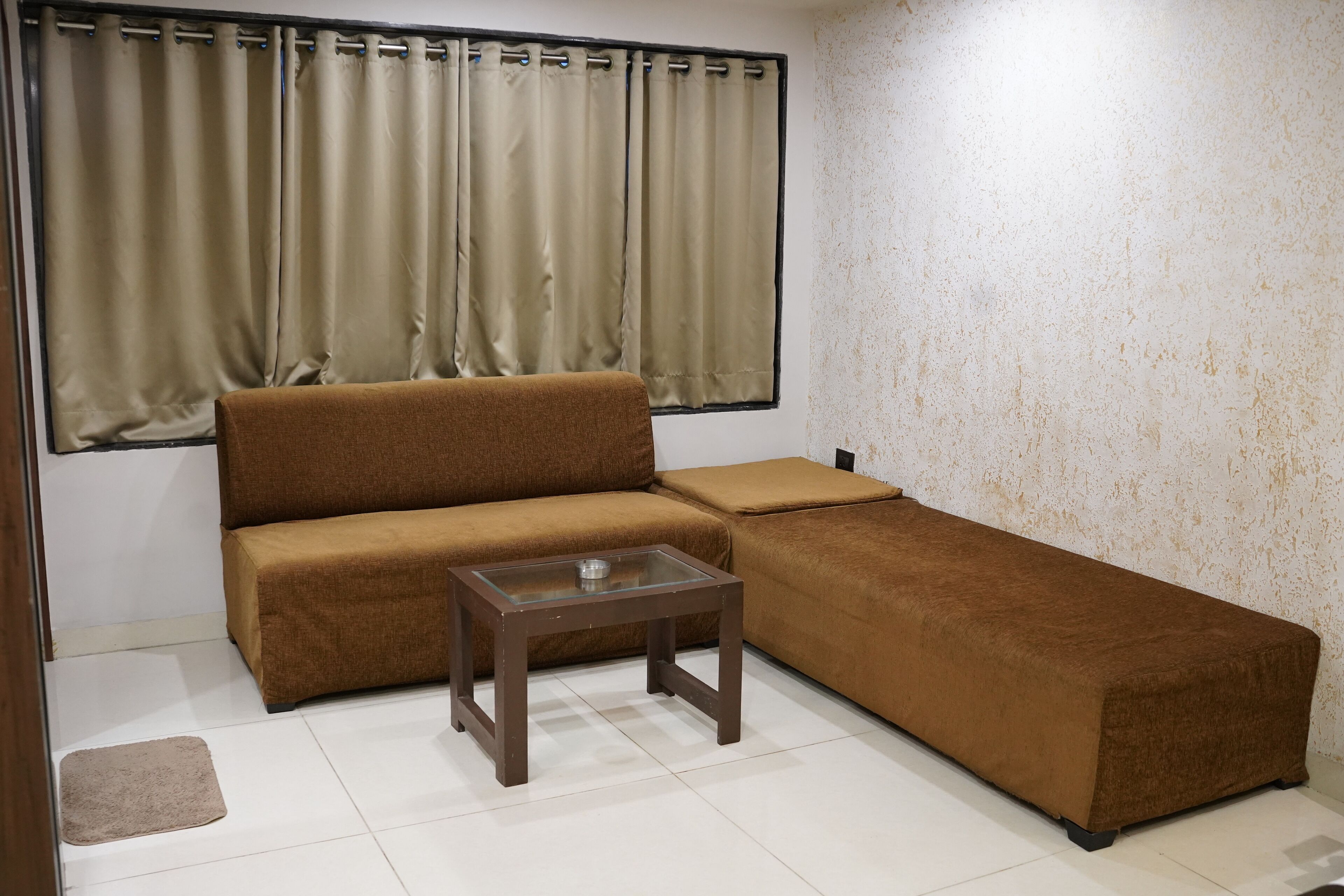 A living room with a brown sofa, a glass coffee table, and beige curtains.