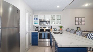 A modern kitchen with stainless steel appliances, white cabinetry, and a marble countertop.