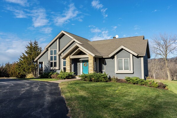 A two-story house with a stone foundation, a blue door, and a well-maintained lawn.