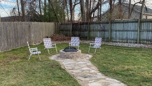 Un jardin avec un sentier en pierre menant à un foyer, entouré de quatre chaises aux motifs décoratifs.