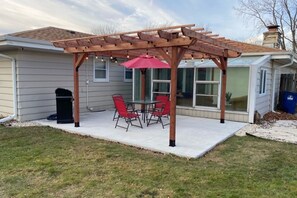 Eine überdachte Terrasse mit Tisch und Stühlen, einem roten Sonnenschirm und einer Holzpergola.