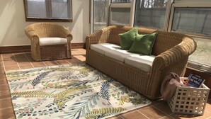 Un salon avec un canapé en osier, un fauteuil assorti et un tapis à motifs floraux.