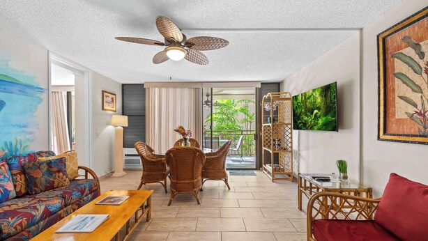 A spacious living area with a ceiling fan, wicker furniture, a red sofa, and a glass table. - Kona Condo- Family Friendly- Fall Sale! (Kailua-Kona)