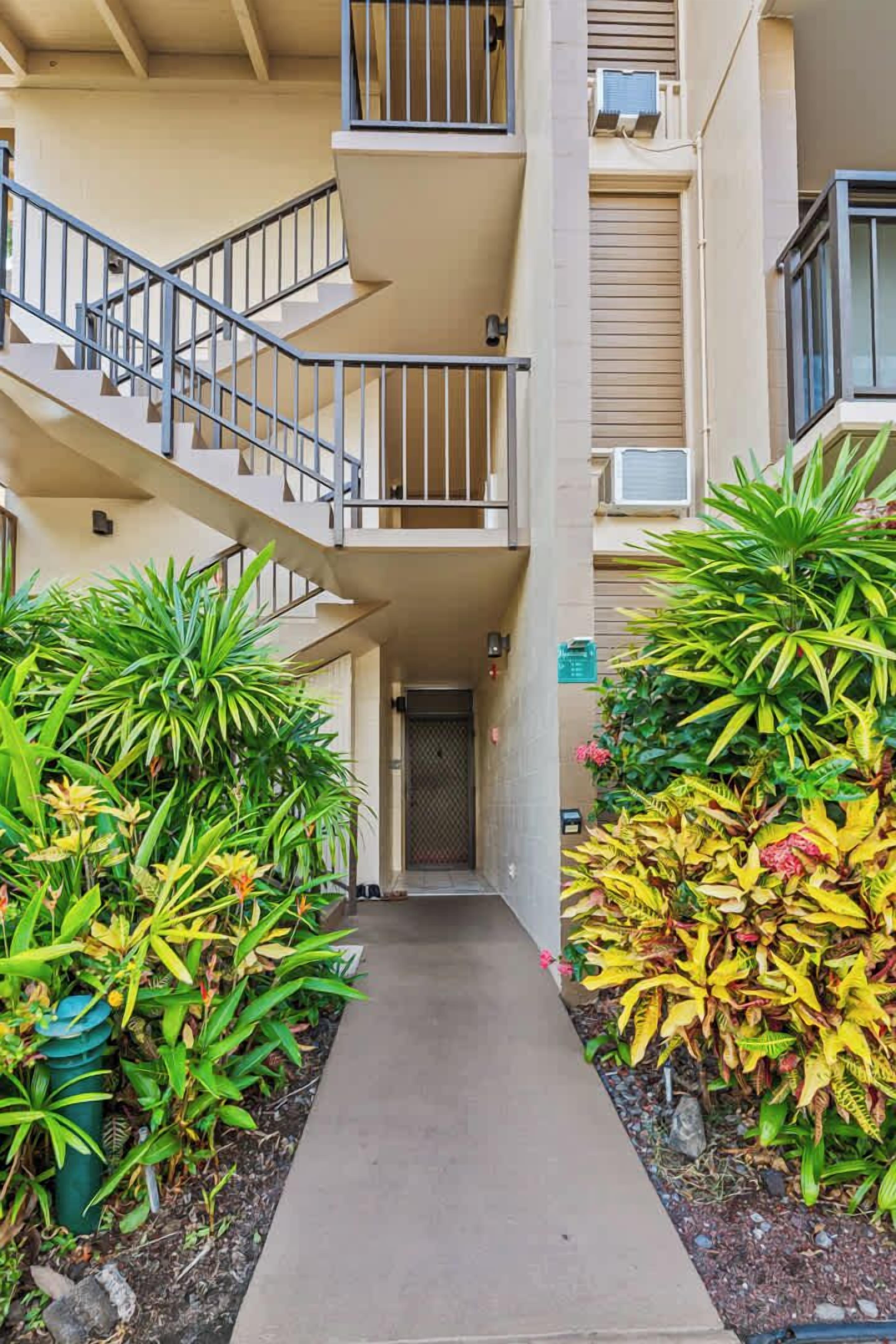 A multi-story building with a central staircase, surrounded by lush greenery and a concrete pathway.