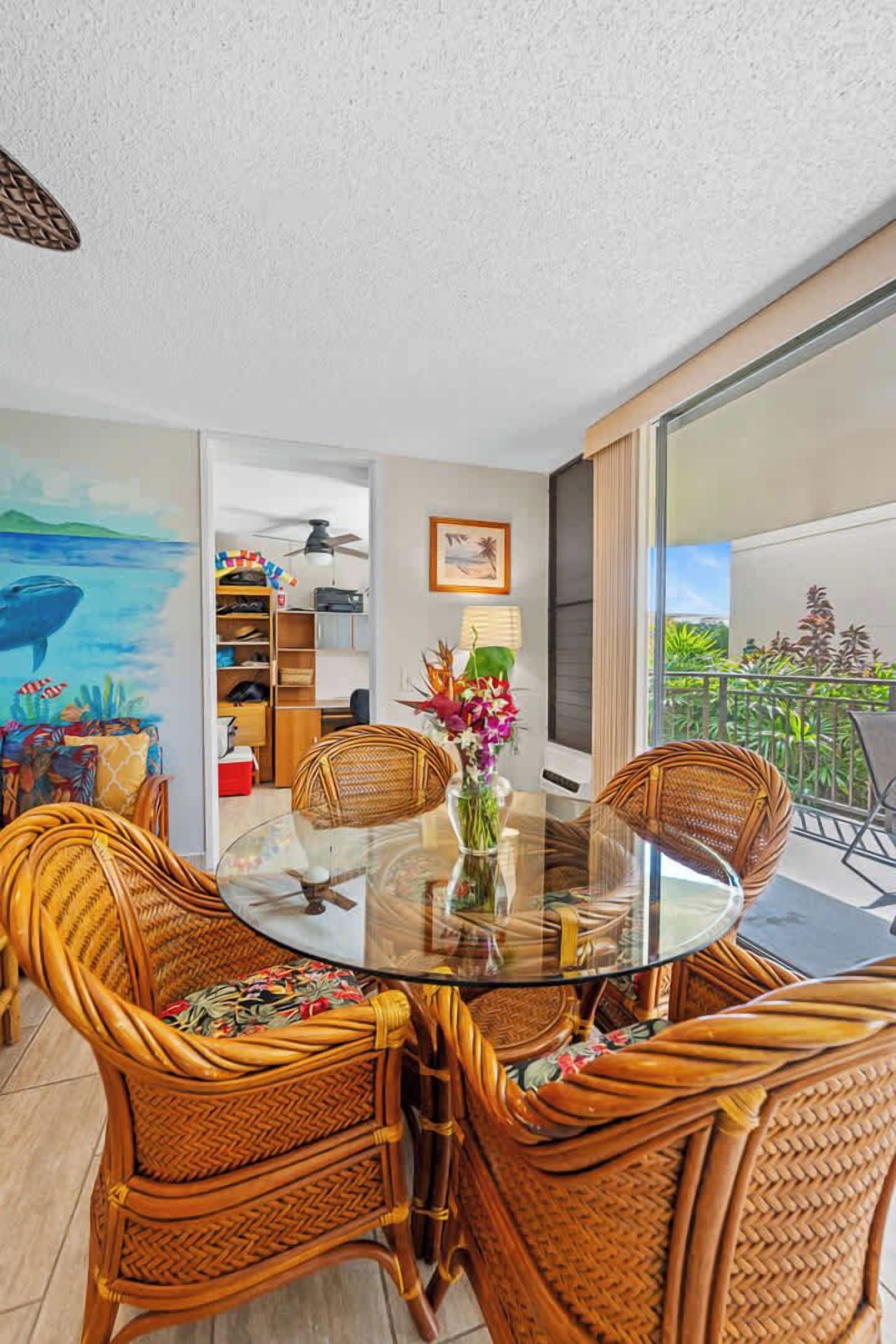 A round glass table surrounded by wicker chairs, a bookshelf, and a painting of a whale on the wall.