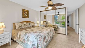 A bedroom with a large bed, a ceiling fan, and a view of a balcony with plants. - Kona Condo- Family Friendly- Fall Sale! (Kailua-Kona)