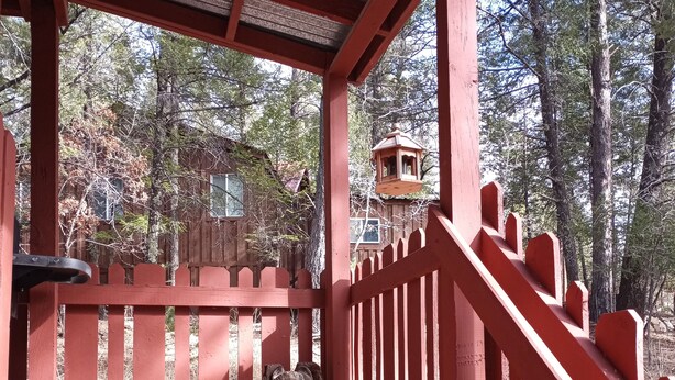A covered wooden deck with a red railing, a stone bench, and a wooden sculpture. - Rustic luxury away from it all (Cloudcroft)