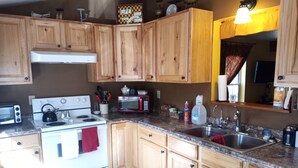 A kitchen with wooden cabinets, a white stove, a microwave, and a sink. - Rustic luxury away from it all (Cloudcroft)