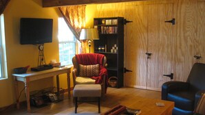 A cozy living room with a wooden floor, a bookshelf, a television, a chair, and a coffee table. - Rustic luxury away from it all (Cloudcroft)
