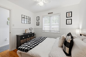 A bedroom with a bed, dresser, and a window with blinds.