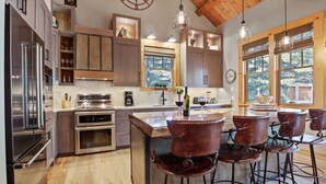 A modern kitchen with stainless steel appliances, wooden cabinetry, and a bar area with metal stools. - RMR: Granite Ridge Homestead 3132 in Teton Village (Teton Village)