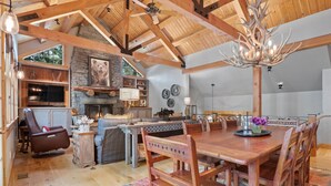 A spacious living area with a wooden dining table, chairs, a fireplace, and a stone wall. - RMR: Granite Ridge Homestead 3132 in Teton Village (Teton Village)