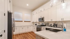 A kitchen with white cabinets, a stainless steel refrigerator, a microwave, and a double sink.