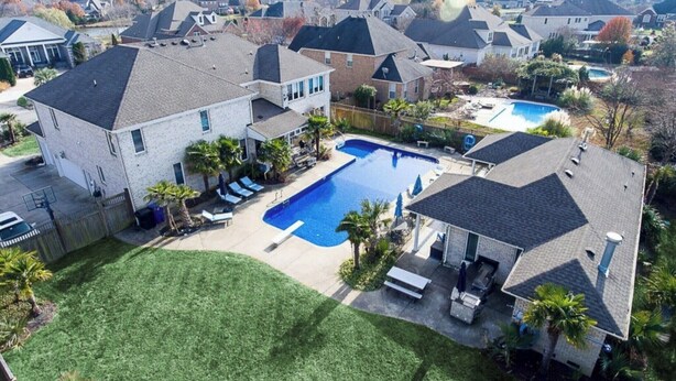 Zona residencial con piscina rodeada de casas, césped cuidado y cielo despejado.