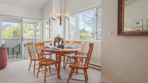 Un espace repas avec une table ronde, des chaises en bois, un lustre et de grandes fenêtres.