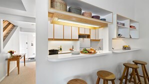 Une cuisine moderne avec des meubles blancs, un four encastré et un comptoir agrémenté de tabourets.