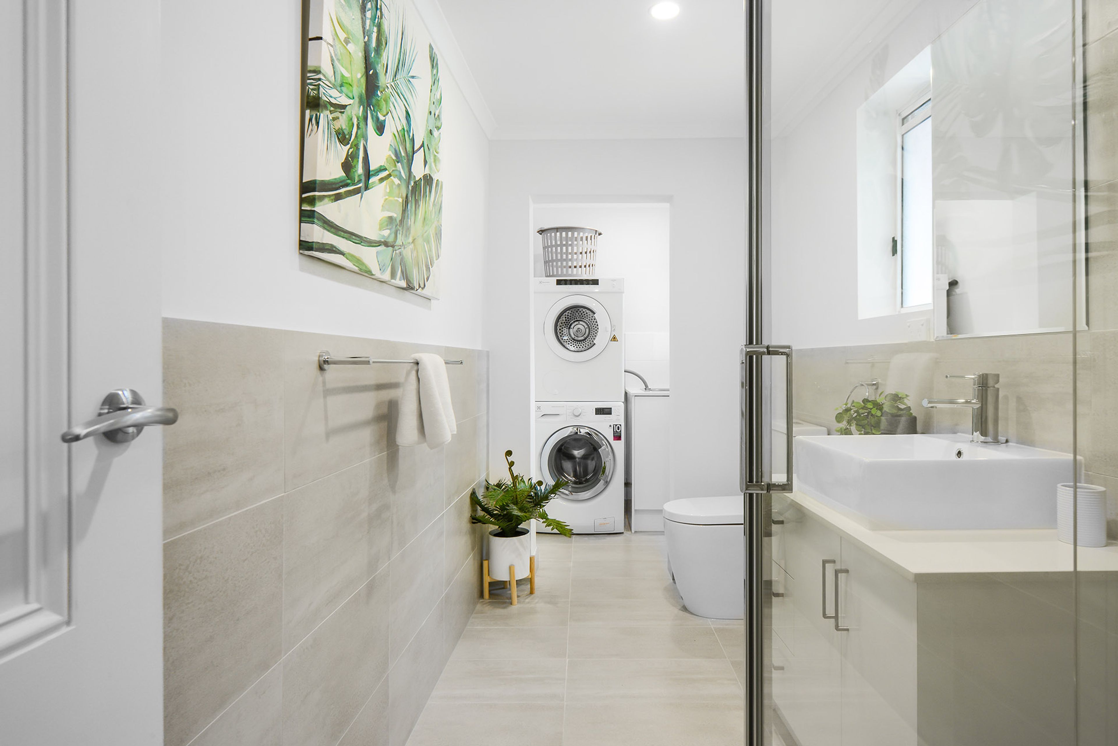 A modern bathroom with a glass shower enclosure, a white sink, and a wall-mounted washing machine.