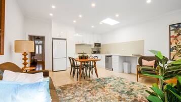 A compact hotel room with a bed, a dining table with chairs, a kitchen area with a refrigerator, microwave, and sink, and a large window.