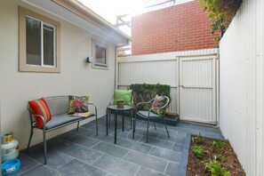 Un espace patio aménagé avec un banc, deux chaises, une petite table et une plante en pot.