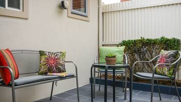 A patio with a metal bench, a small round table, and two chairs, each with a cushion.