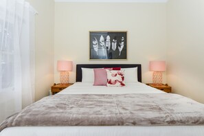 A hotel room with a large bed, two bedside tables with lamps, a framed artwork above the bed, and sheer curtains on the window. - Carlton Terrace Pet Friendly (Carlton)