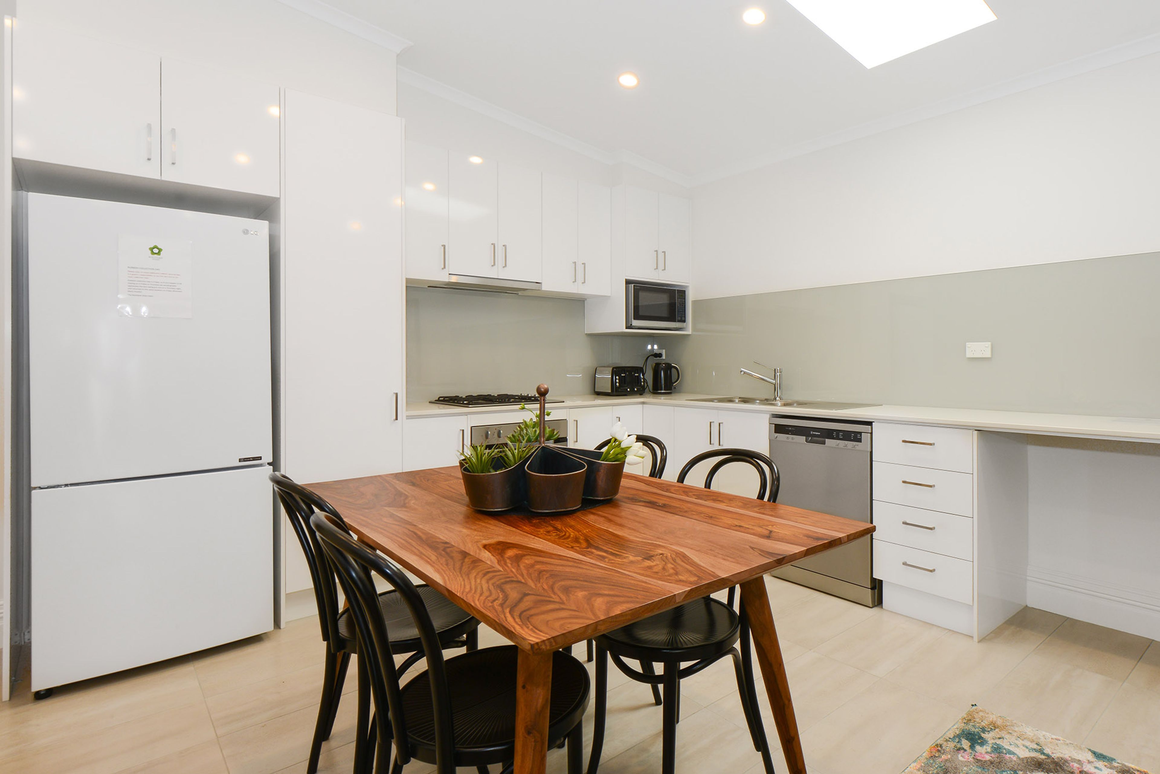 A modern kitchen with white cabinets, a wooden dining table, and a built-in microwave.