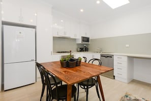 A modern kitchen with white cabinets, a wooden dining table, and a built-in microwave. - Carlton Terrace Pet Friendly (Carlton)