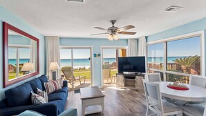 Un salón amplio con un televisor grande, un ventilador de techo y un balcón con vistas al océano.