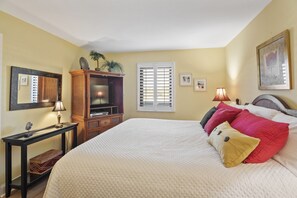 A bedroom with a large bed, a wooden dresser, a television, and a window with shutters.