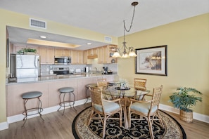 A kitchen with wooden cabinets, a stainless steel refrigerator, a microwave, and a dining area with a glass table and wicker chairs.