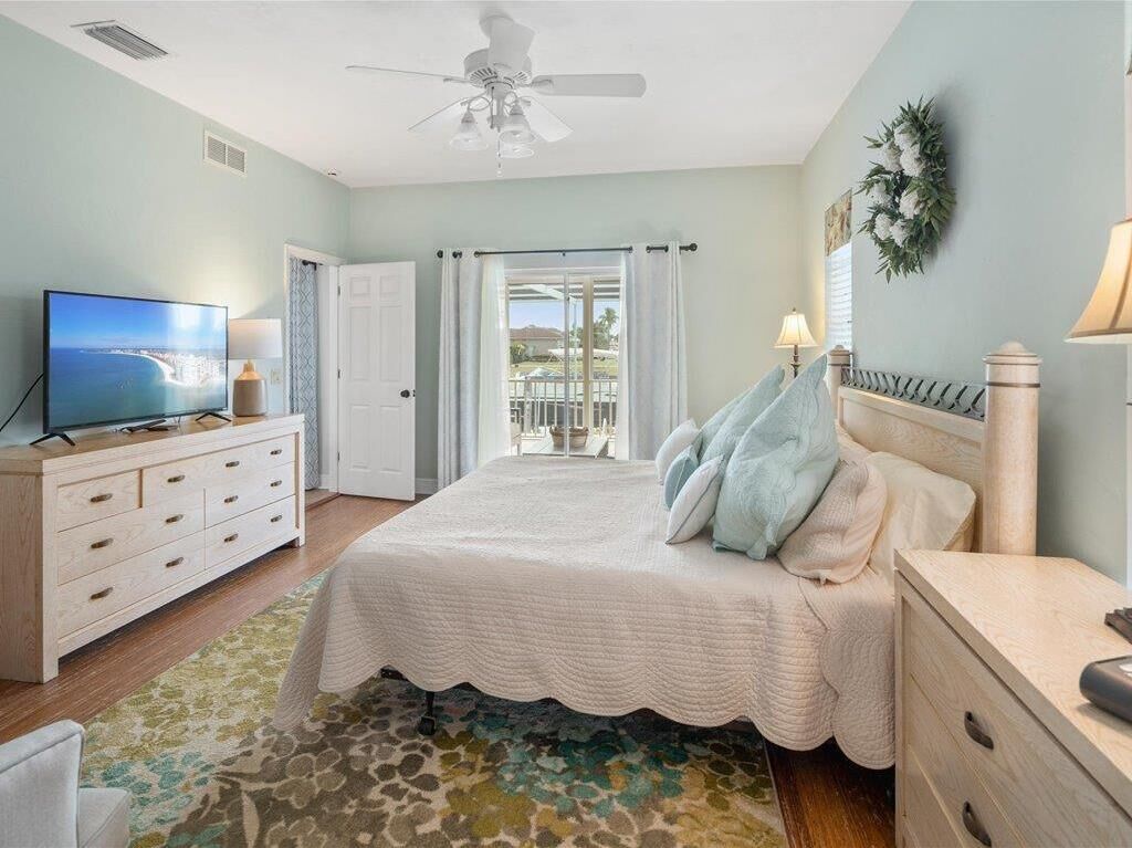 A bedroom with a bed, a dresser, a television, and a view of the outdoors through a sliding door.