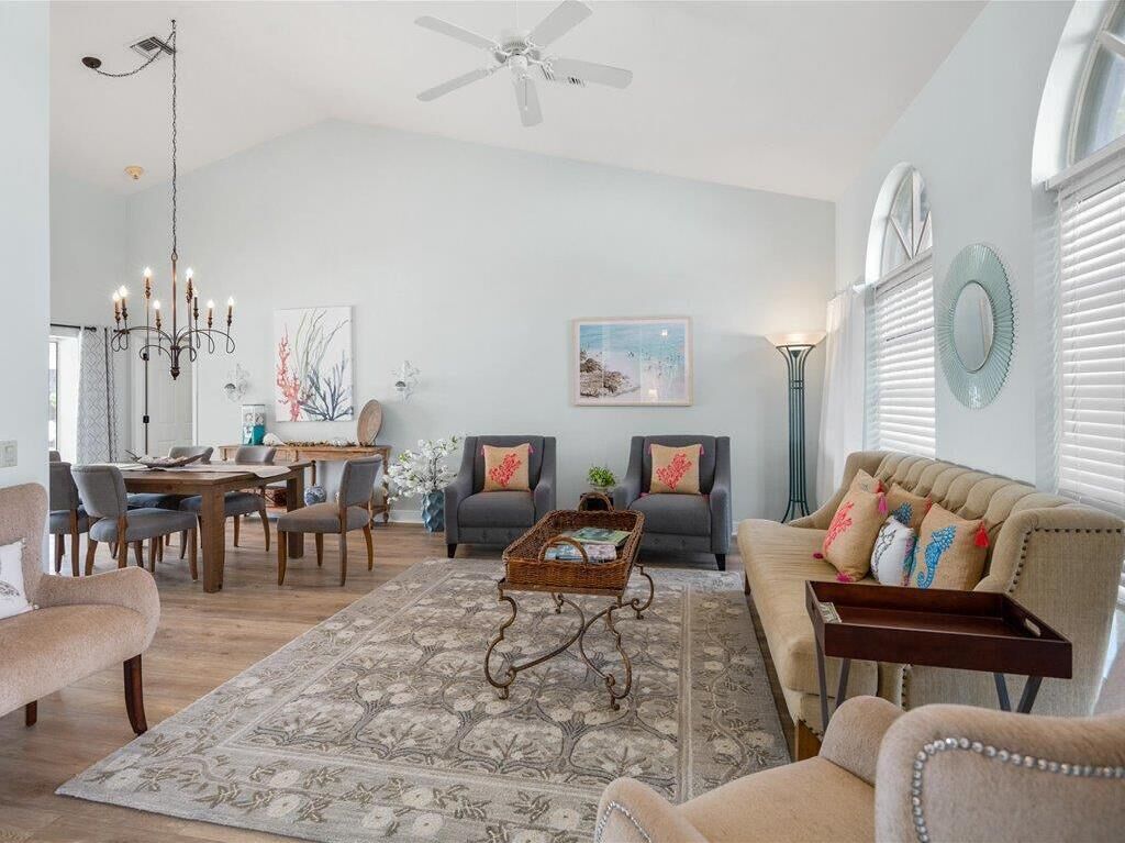A spacious living room with a high ceiling, a chandelier, a dining area with a wooden table and chairs, and a sofa with decorative pillows.