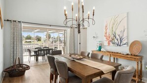 A dining area with a wooden table, six chairs, a chandelier, and a view through a glass door. - Waterfront 3BR home with heated pool in Marco Island. (Marco Island)