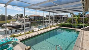 A covered swimming pool with clear water, a pool ladder, and lounge chairs. - Waterfront 3BR home with heated pool in Marco Island. (Marco Island)
