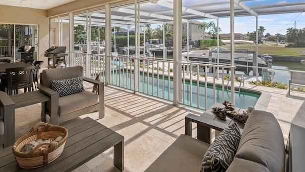 A covered outdoor area with a pool, lounge chairs, and a grill. - Waterfront 3BR home with heated pool in Marco Island. (Marco Island)