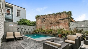 A backyard with a swimming pool, wicker furniture, and a brick wall. - Spacious Condo w/ Pool & Courtyard Near French Quarter (New Orleans)