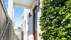 A narrow, covered walkway leading to a white building with a wooden door and a small porch. - Spacious Condo w/ Pool & Courtyard Near French Quarter (New Orleans)