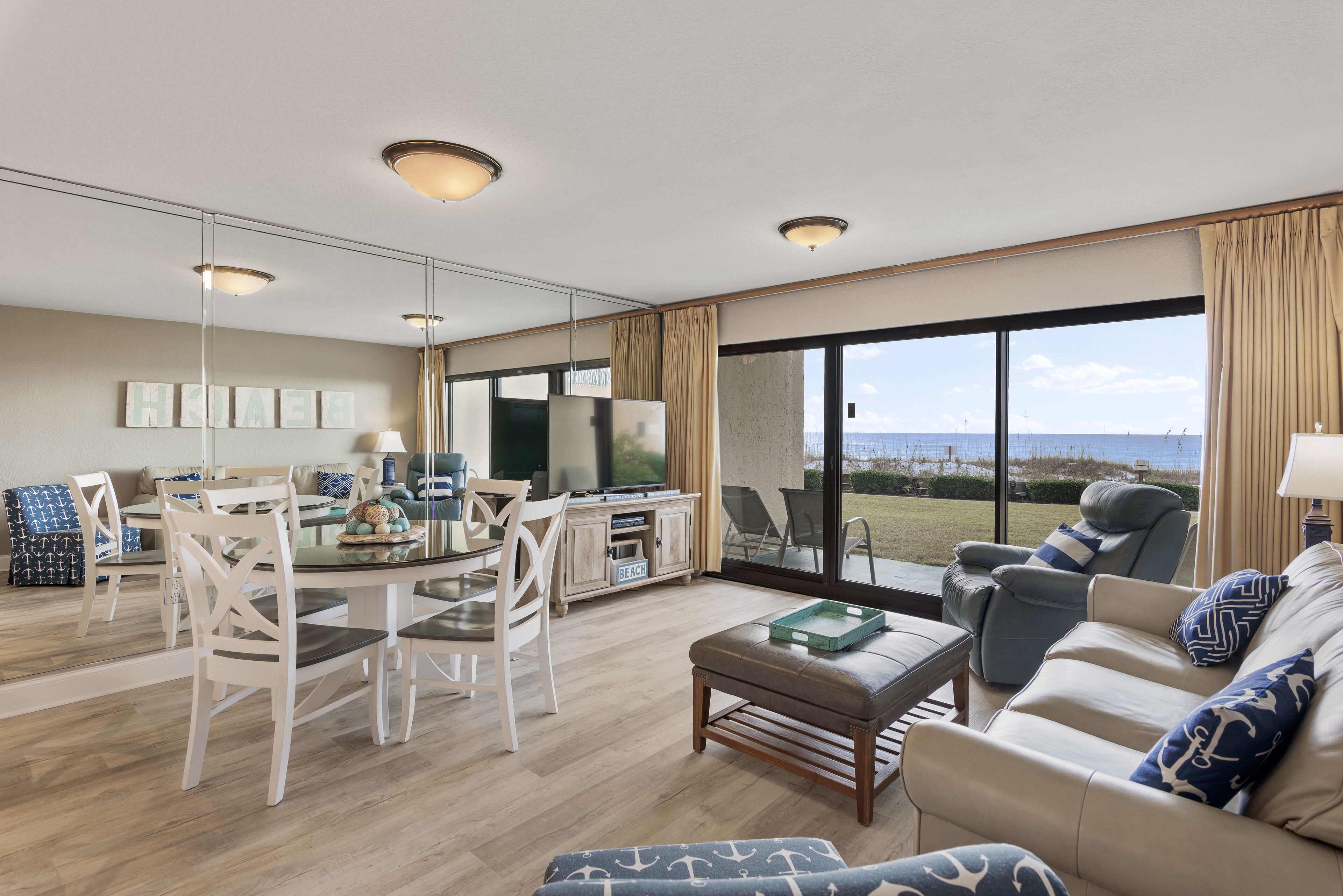 A spacious living room with a dining area, large windows with a view, and a beach-themed decor.