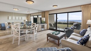 Ein geräumiges Wohnzimmer mit Essbereich, großen Fenstern und Meerblick, sowie einer Strand-Deko.