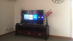Un televisor de pantalla plana sobre un soporte de madera y un reloj en la pared.